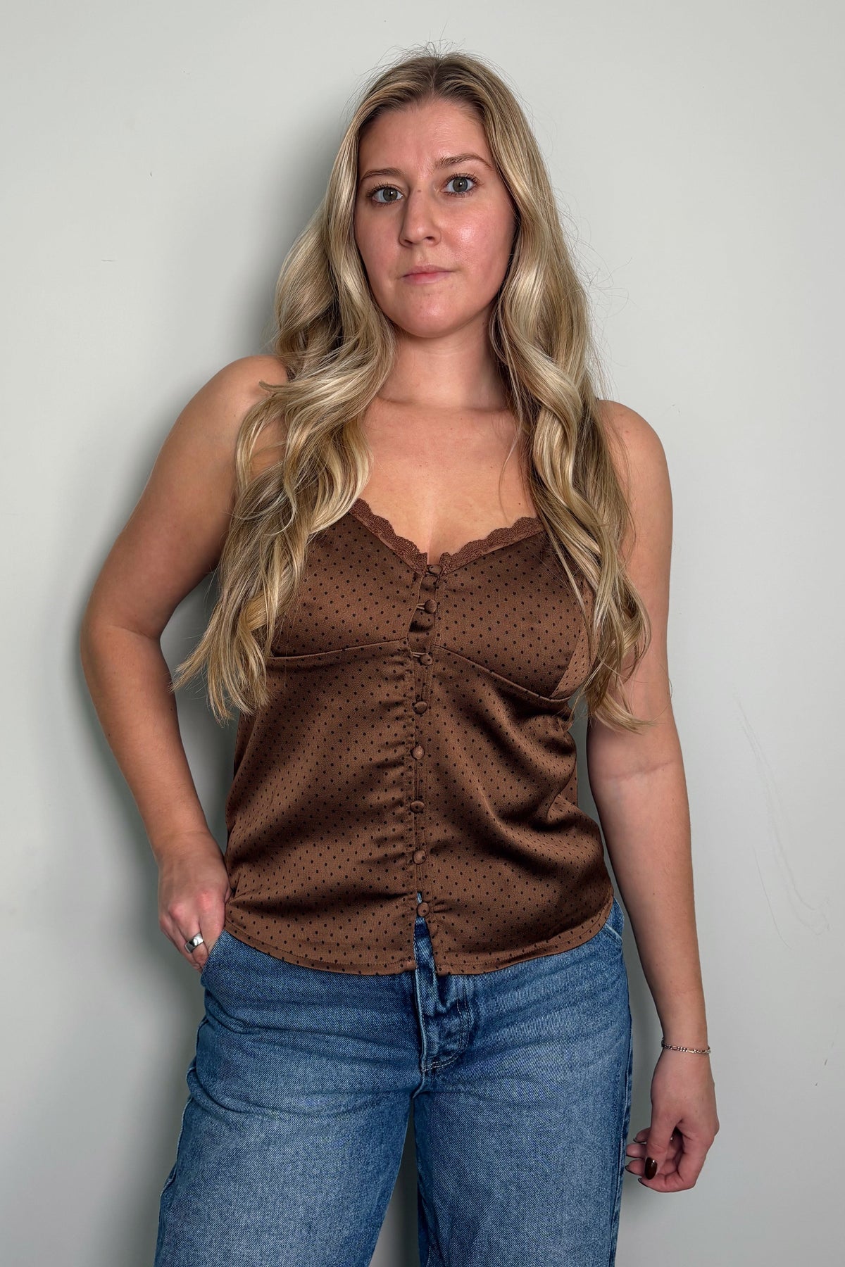 Front view of a model in the Delancey brown polka dot cami with delicate lace trim, button-front detail, and adjustable straps