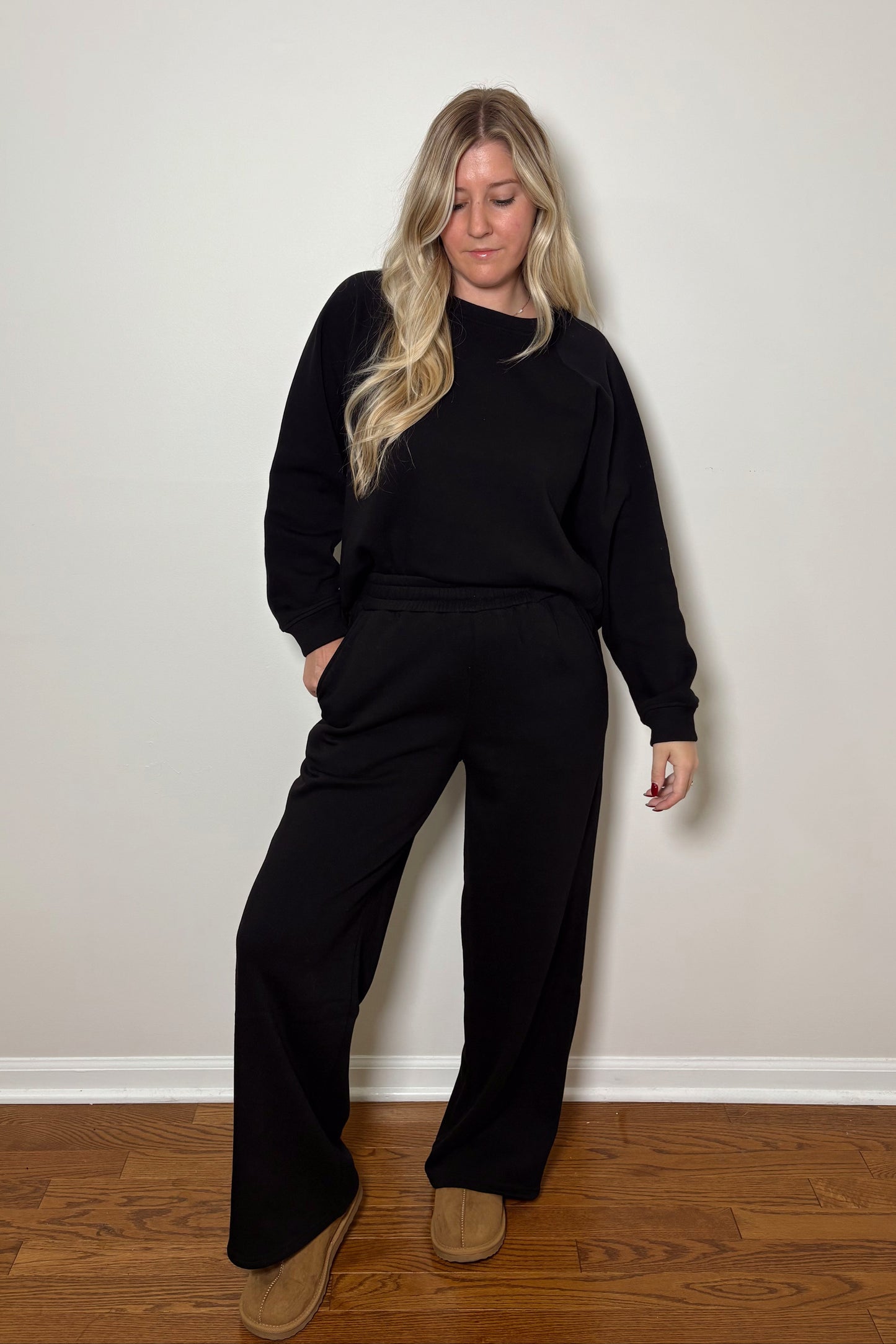 Person wearing a black lounge set standing against a plain wall.