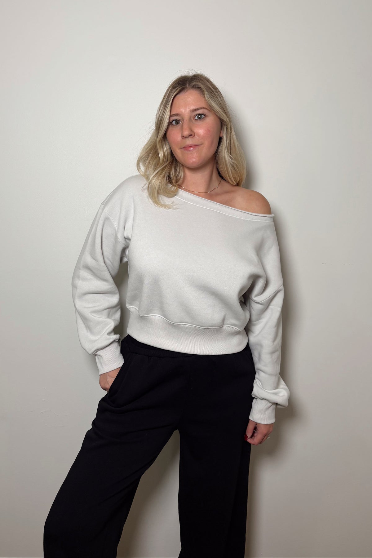 Haven stone cropped boatneck pullover styled off one shoulder with black pants, showing long sleeves and ribbed cuffs.

