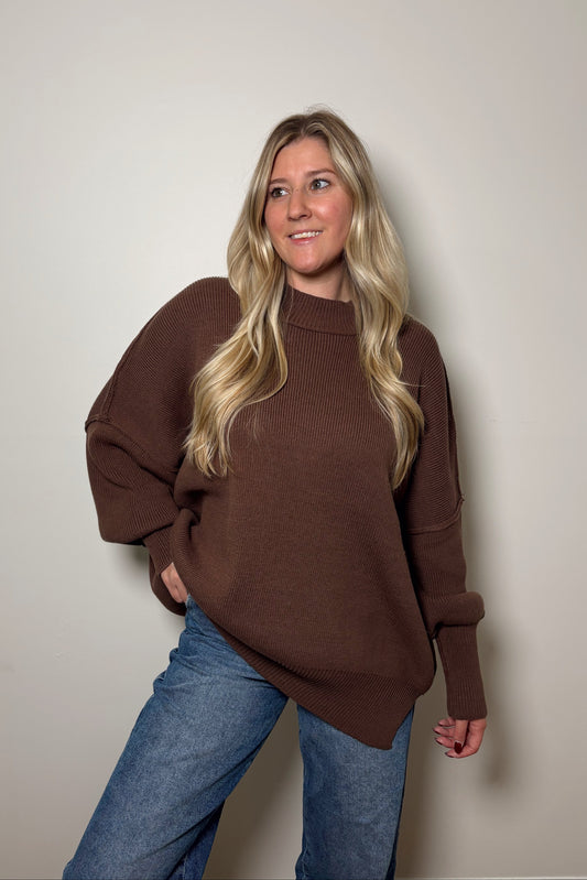 Woman wearing a brown sweater and blue jeans against a plain background