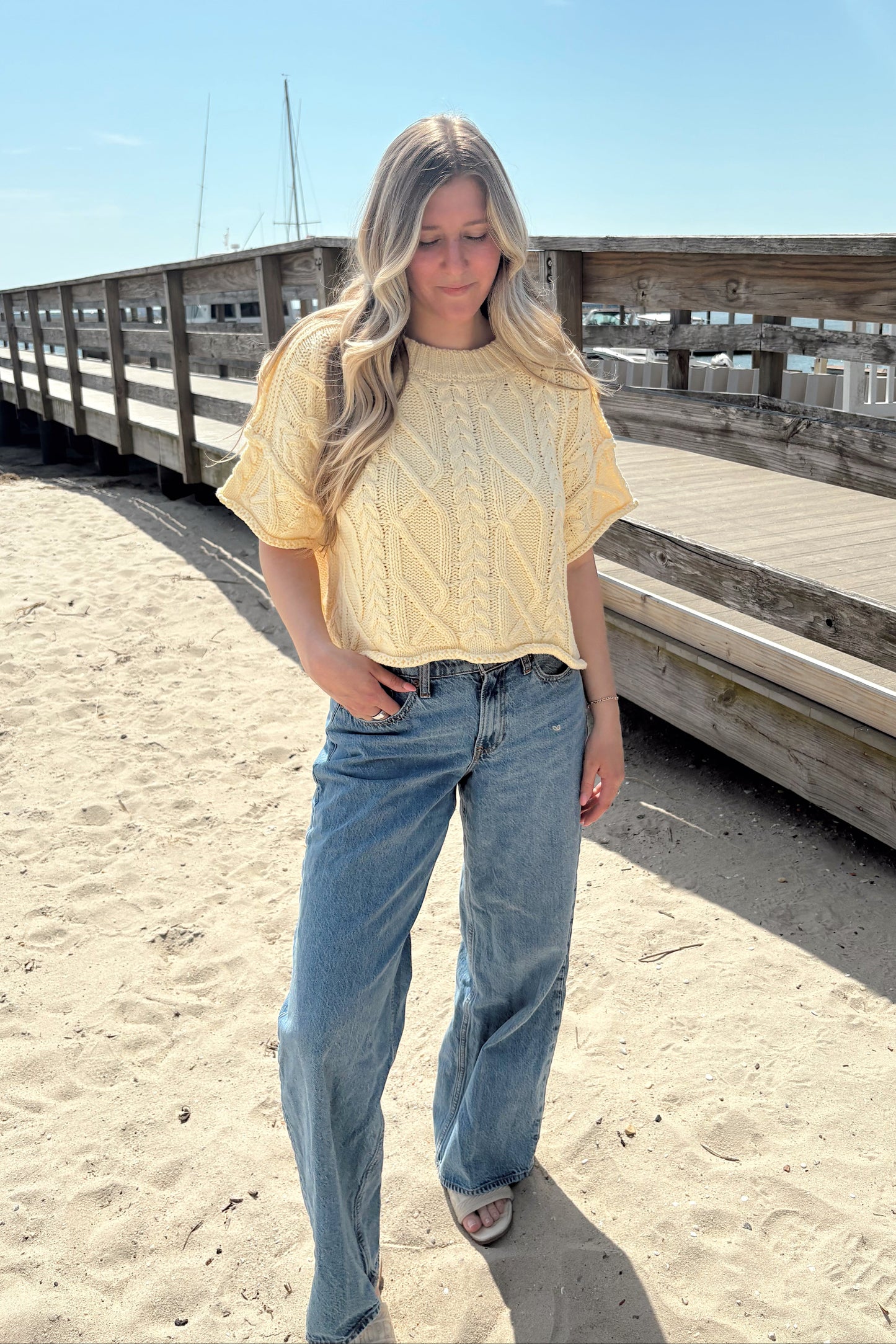 Person standing on a sandy beach with a wooden structure in the background