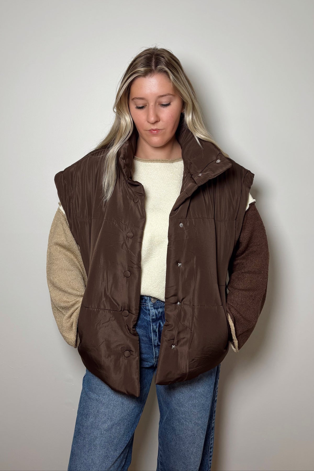 Front view of the Parker brown oversized puffer vest worn open with both hands in the side pockets.

