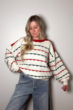 Person wearing a white sweater with red and black stripes against a plain background