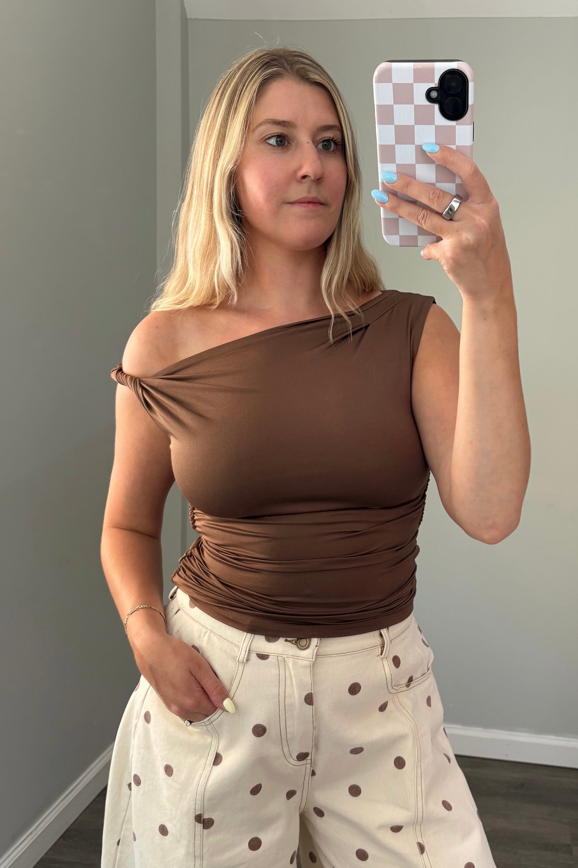 Woman taking a mirror selfie wearing a brown top and polka dot pants.