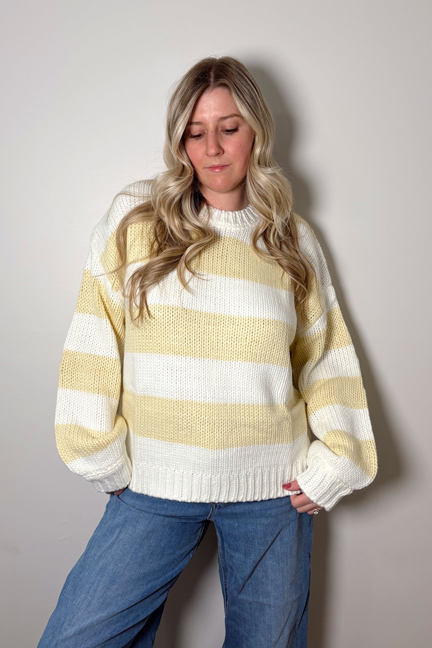 Person wearing a yellow and white striped sweater with blue jeans against a plain background