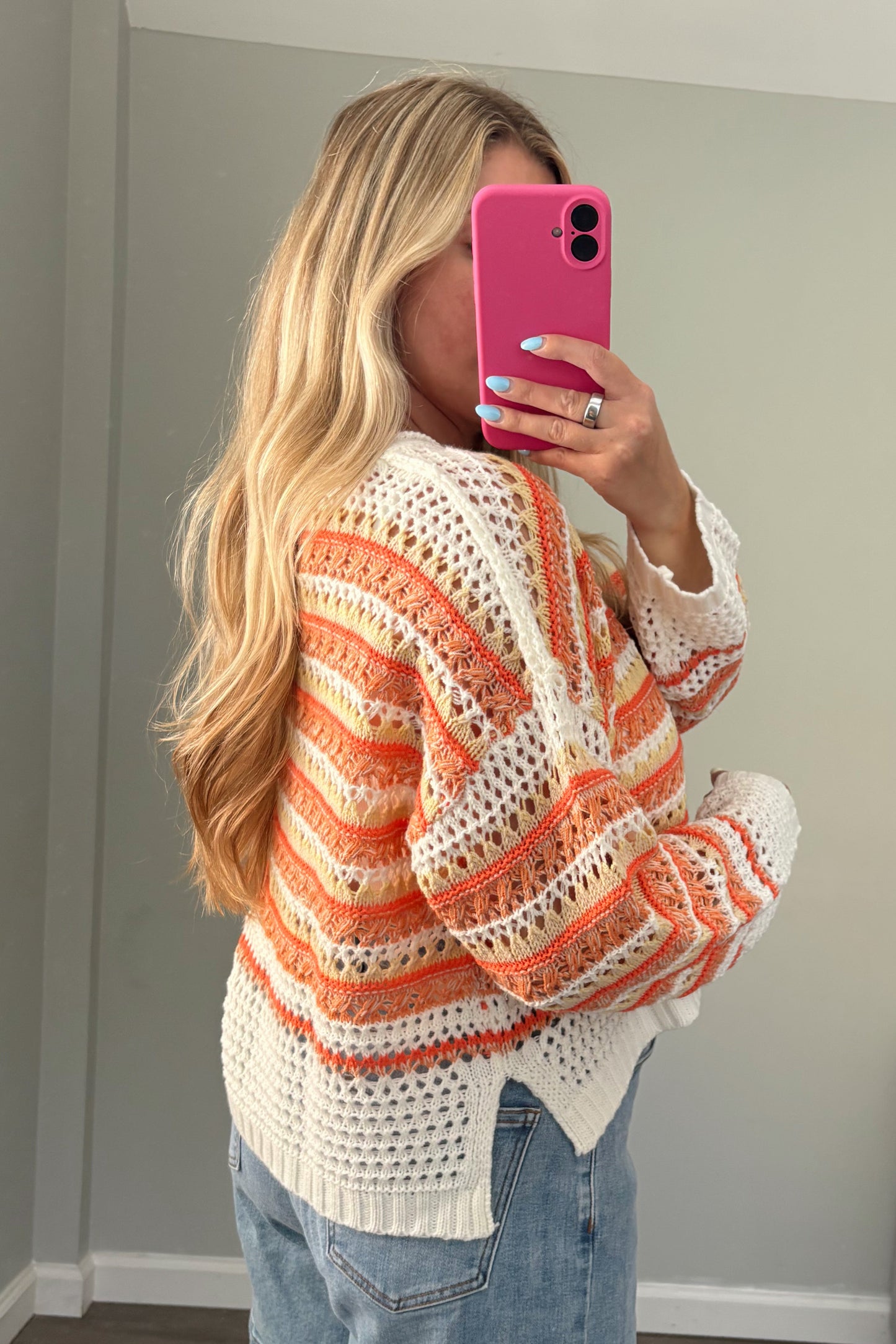 Person wearing a colorful striped sweater and denim shorts, taking a mirror selfie.