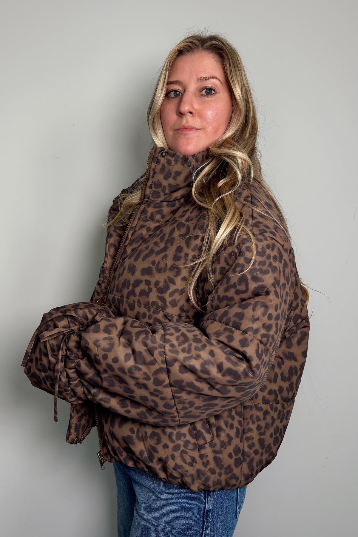 Side view of a model in the zipped-up Coco leopard puffer jacket with drawstring ties at the sleeves