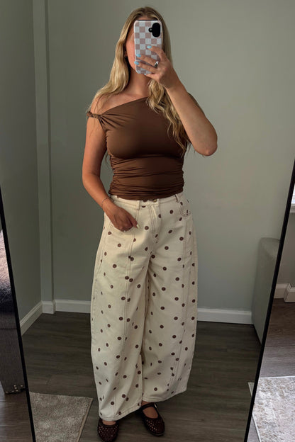 Person wearing a brown top and white polka dot pants taking a mirror selfie.