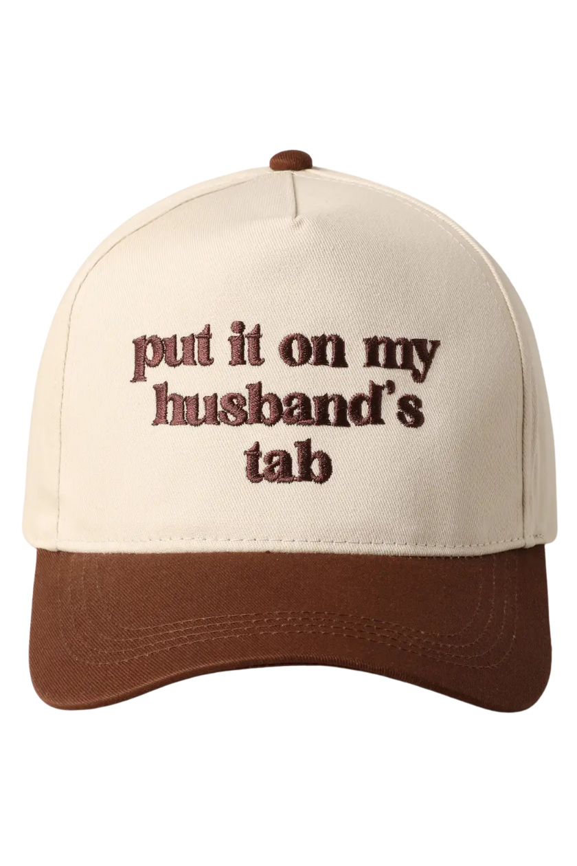 A baseball cap with an off-white crown and a brown visor, featuring the phrase 'put it on my husband's tab' embroidered in brown on the front.