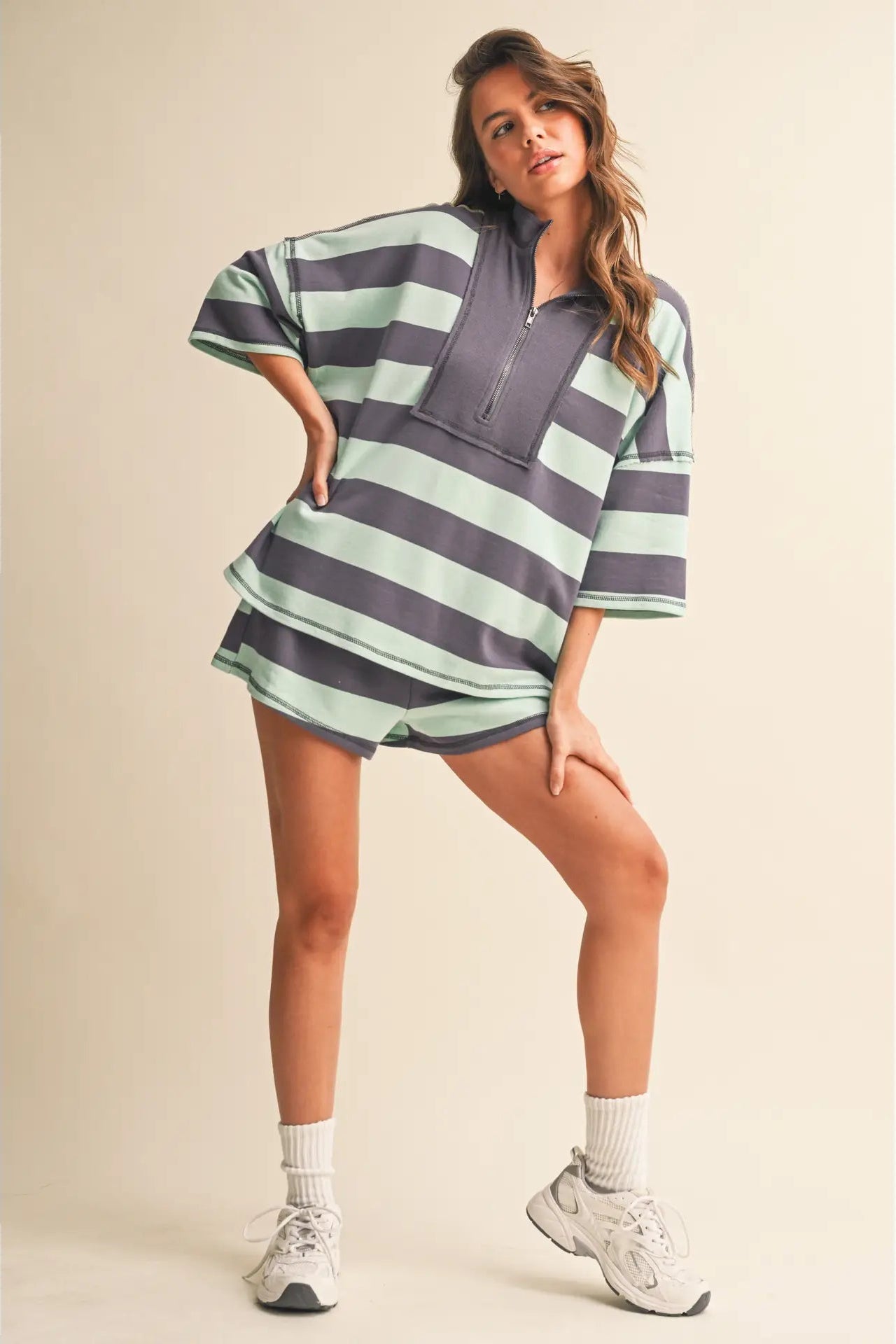 Woman wearing a striped outfit with a half zip on a beige background