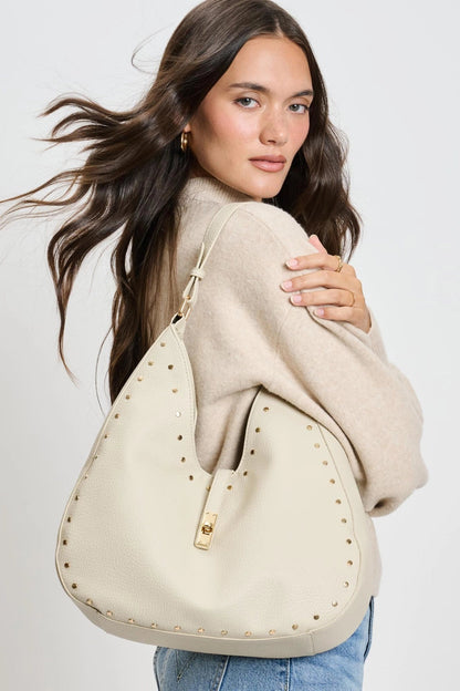 Woman holding a beige handbag with gold studs against a white background