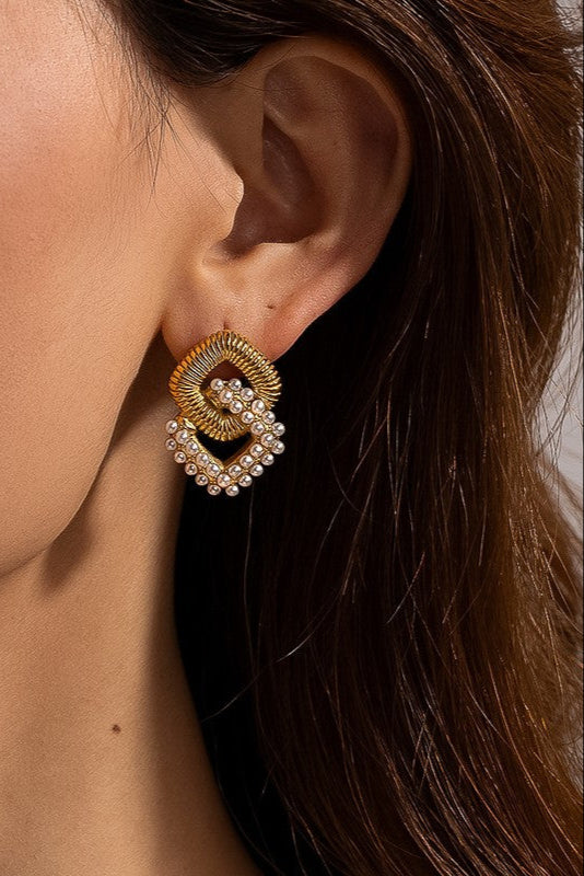 Close-up of a Cometa earring worn on an ear, showing a textured gold-tone link interlocked with a white faux pearl loop.

