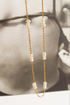 Close-up of the Leilani necklace showing white pearl clusters spaced along a delicate gold-tone chain against a black-and-white photo.

