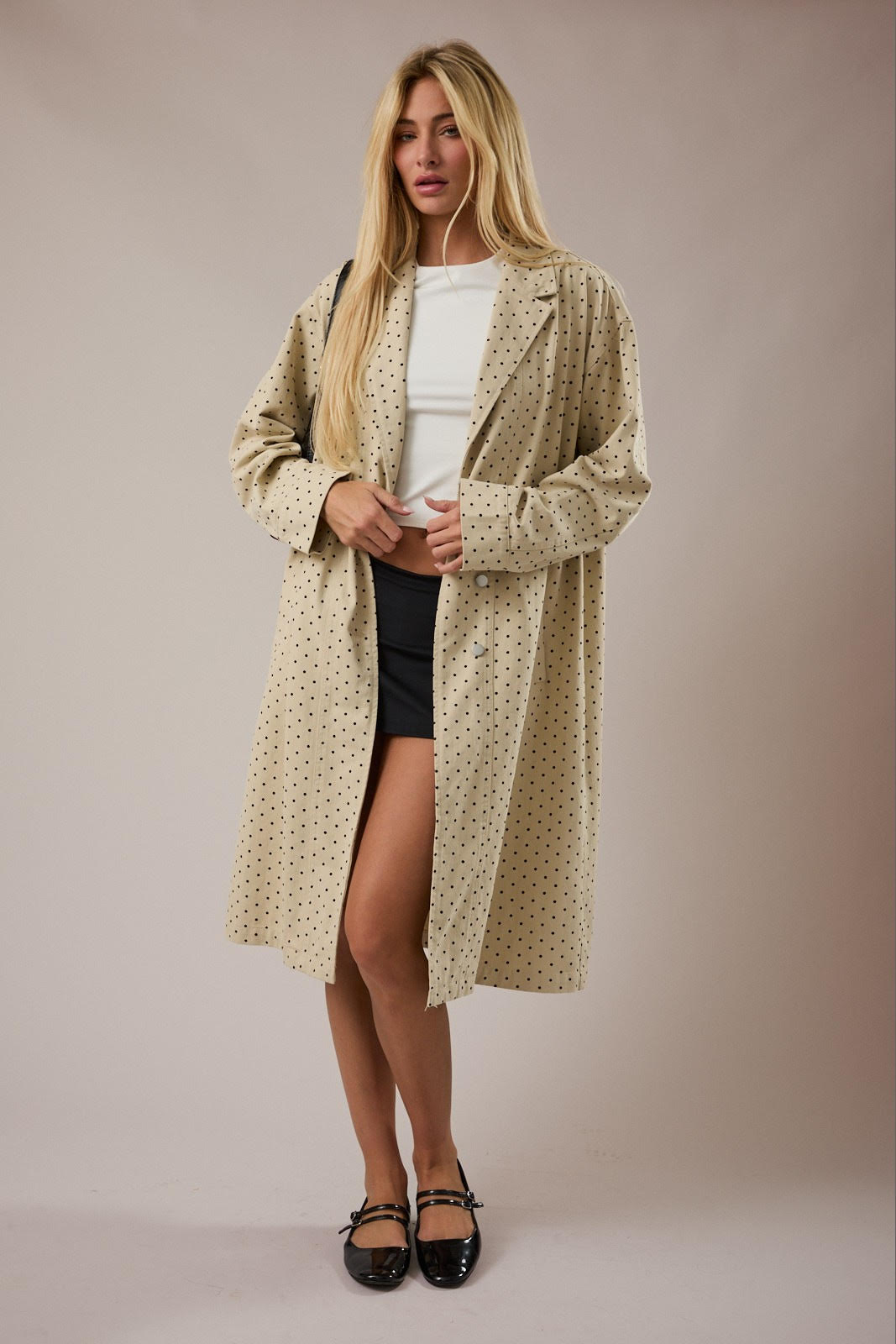 Woman wearing a long beige patterned coat over a white top and black skirt on a plain background