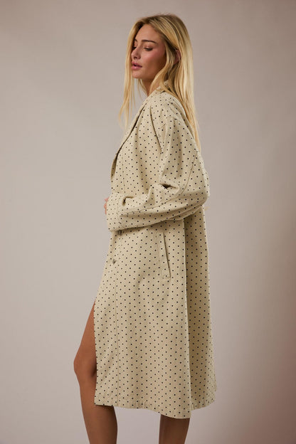 Woman wearing a beige polka dot jacket against a plain background